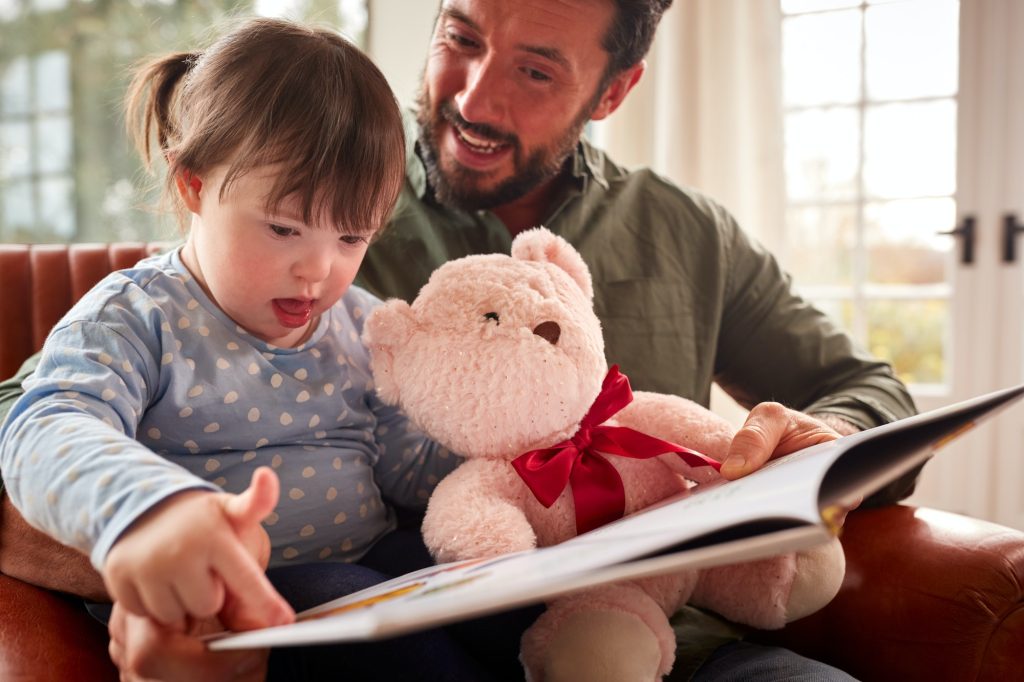 Father With Down Syndrome Daughter Reading Book At Home Together