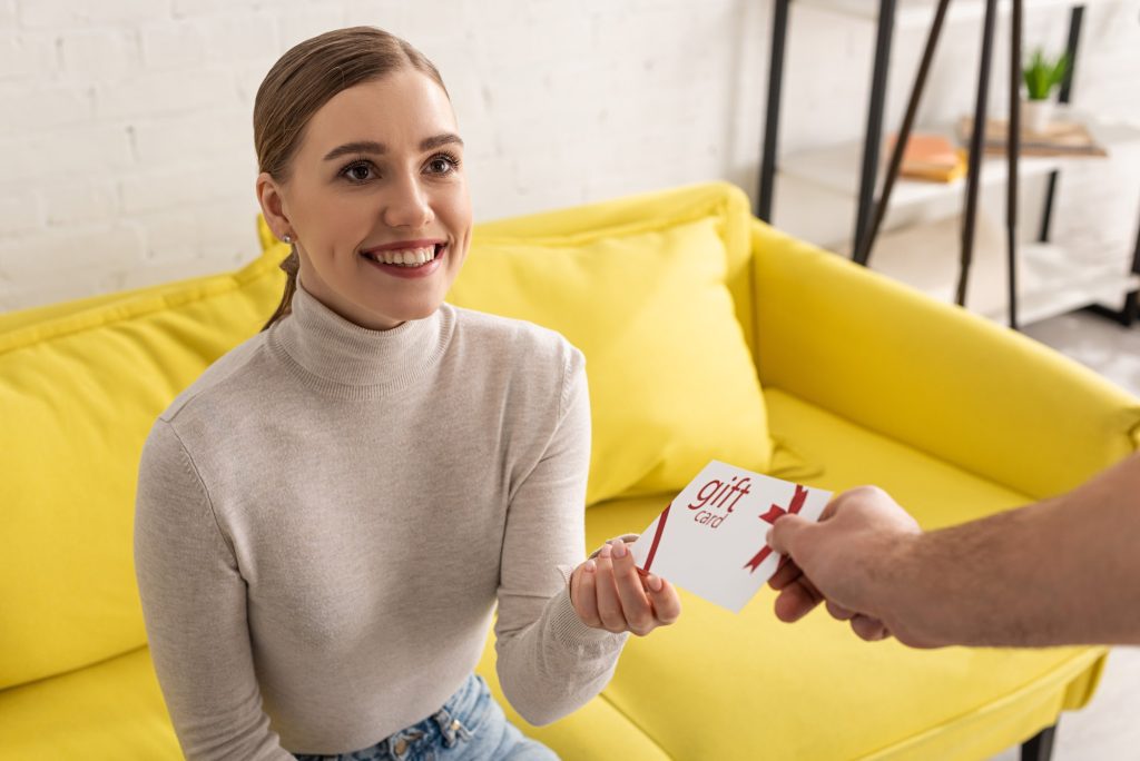 Man giving gift card to smiling girlfriend on couch